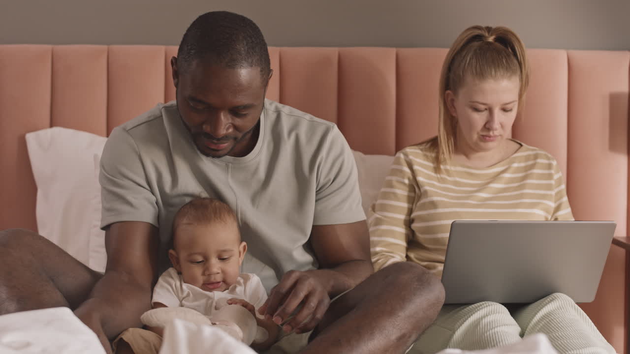 Pai com bebê e mulher na cama