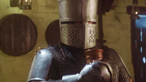 knight drinks and straw stacks under visor in tavern. strong medieval warrior enjoys alcohol beverage through dry hay stem in pub. face armour problems