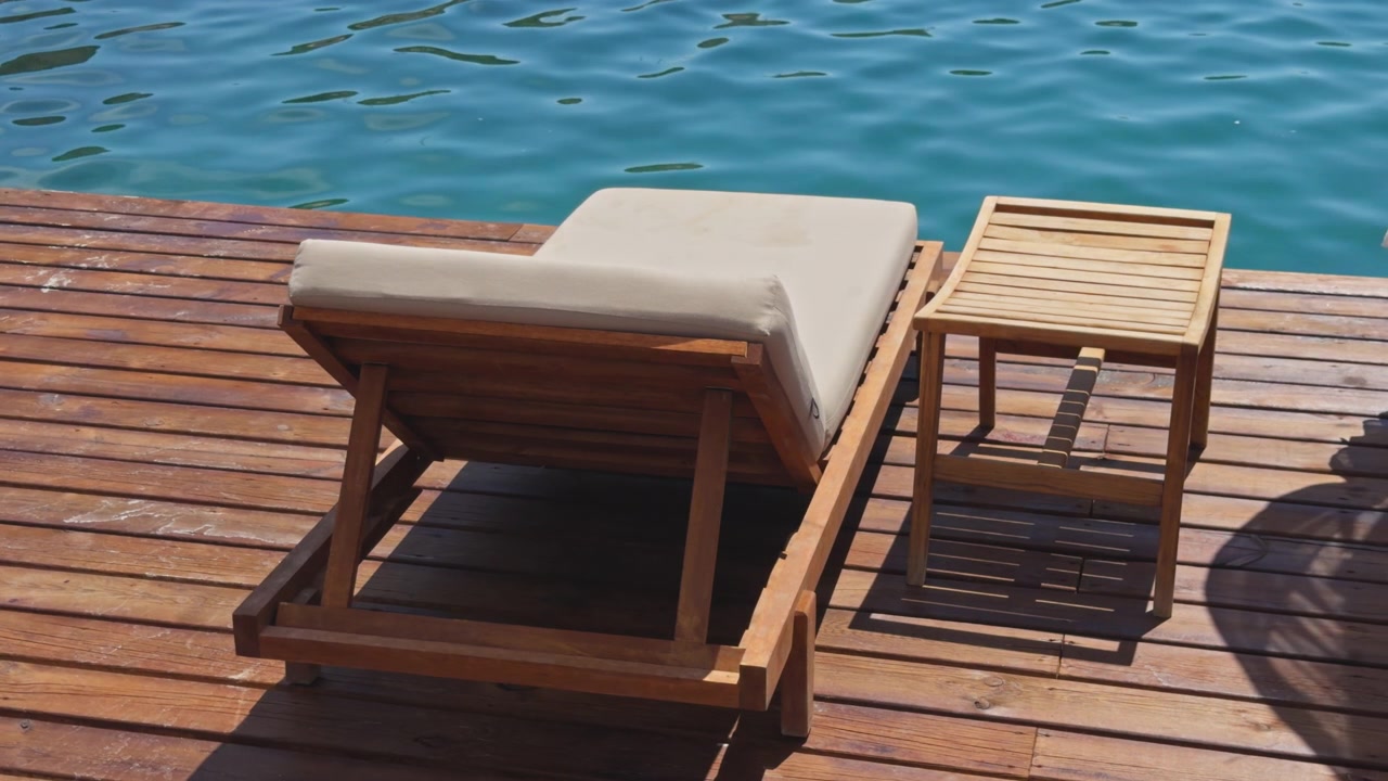 Wide shot of empty sun lounger and side table on sunny wooden dock overlooking bright blue sea, luxury beach club setting, Mediterranean coast, Turkey.