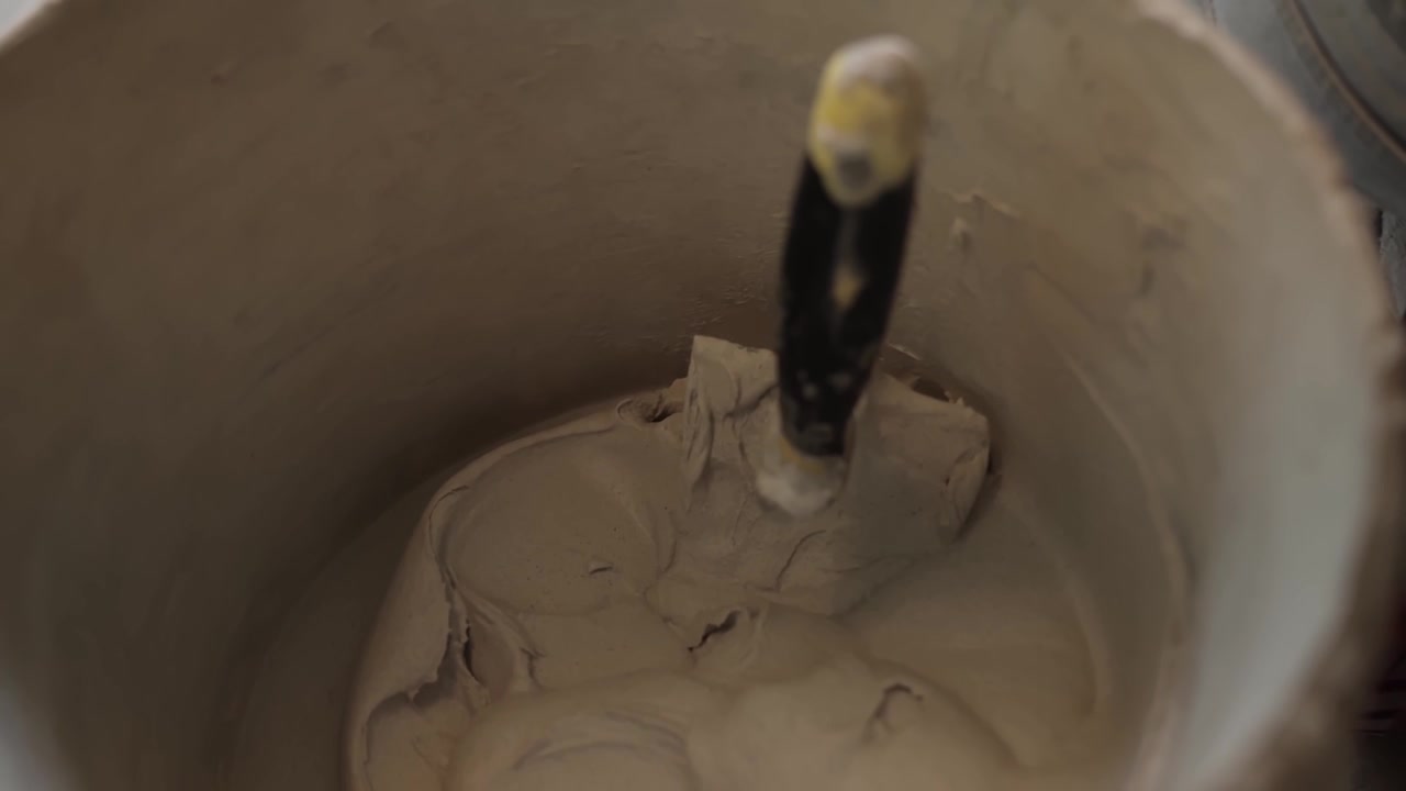 Primo piano all'interno di un secchio di adesivo per piastrelle preparato con una cazzuola appoggiata nella miscela densa durante la posa di un pavimento interno