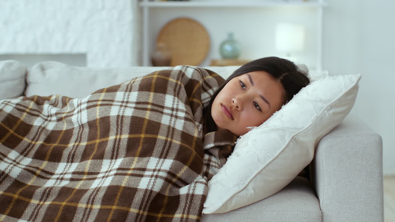 Woman resting on couch covered in blanket
