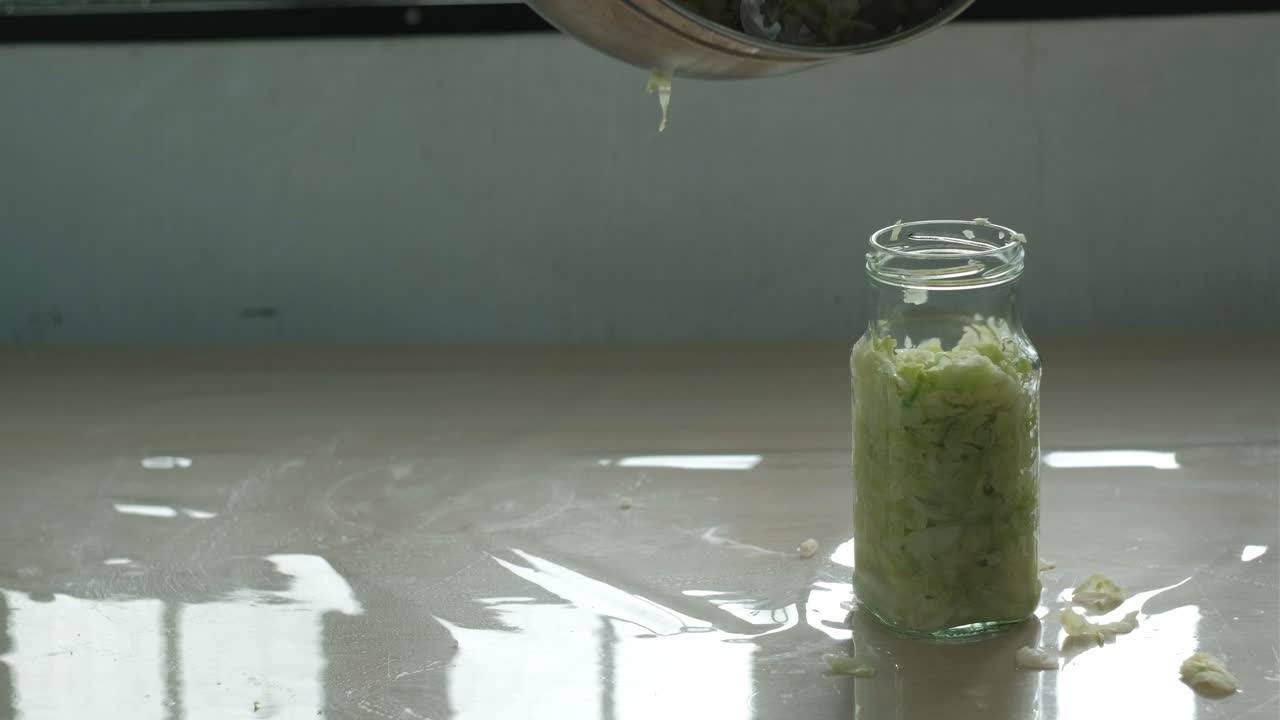 Pouring shredded cabbage juice out of stainless steel bowl into glass jar of Sauerkraut -static close-up shot