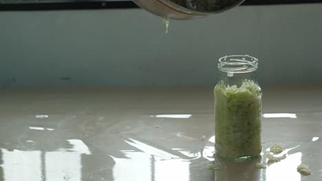 pouring shredded cabbage juice out of stainless steel bowl into glass jar of sauerkraut -static close-up shot