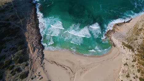 Strandbucht-Aus-Der-Vogelperspektive-Mit-Großen-Wellen,-Klarem-Türkisfarbenem-Meerwasser,-Grünen-Hügeln-Und-Weißem-Sand