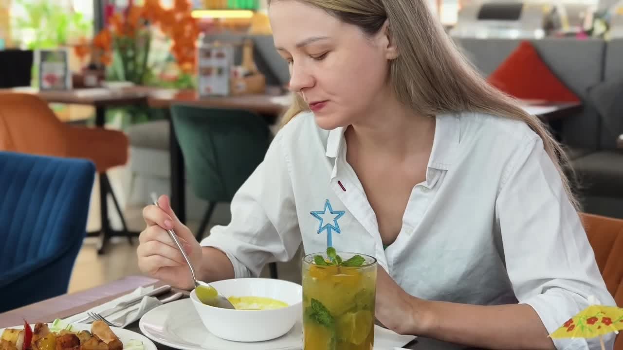 mujer comiendo sopa y bebiendo un cóctel en un café
