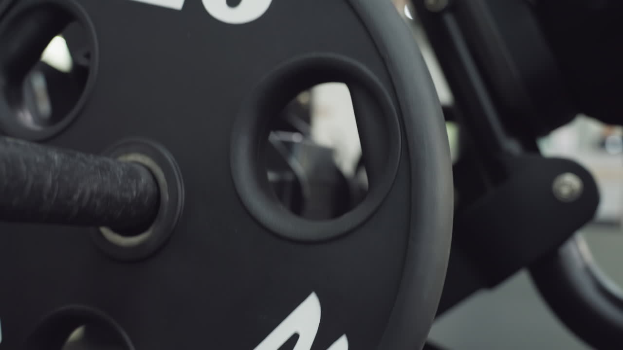 Black five kilo weight plate sliding along metal bar as muscle enthusiast adjusts resistance on chest press machine in bright modern gym, close up showing textured surface details and rotating motion