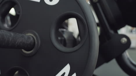 black five kilo weight plate sliding along metal bar as muscle enthusiast adjusts resistance on chest press machine in bright modern gym, close up showing textured surface details and rotating motion