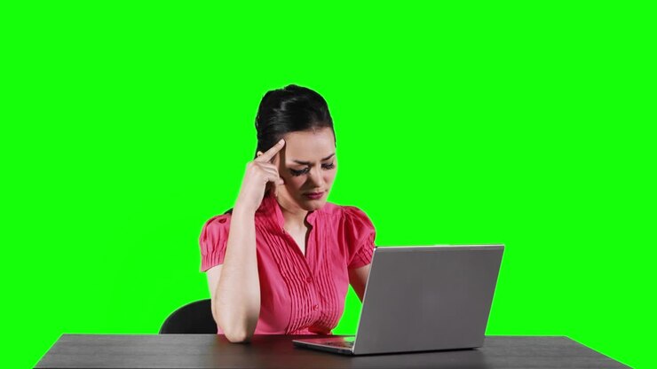 Junge Mitarbeiterin arbeitet mit einem Laptop auf dem Tisch und bekommt eine Idee, gefilmt in 4K-Auflösung mit grünem Bildschirmhintergrund.