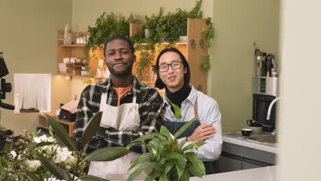 Two-Multiethnic-Waiters-With-Crossed-Arms-Looking-At-Camera-While-Standing-Behind-Counter-In-A-Coffee-Shop