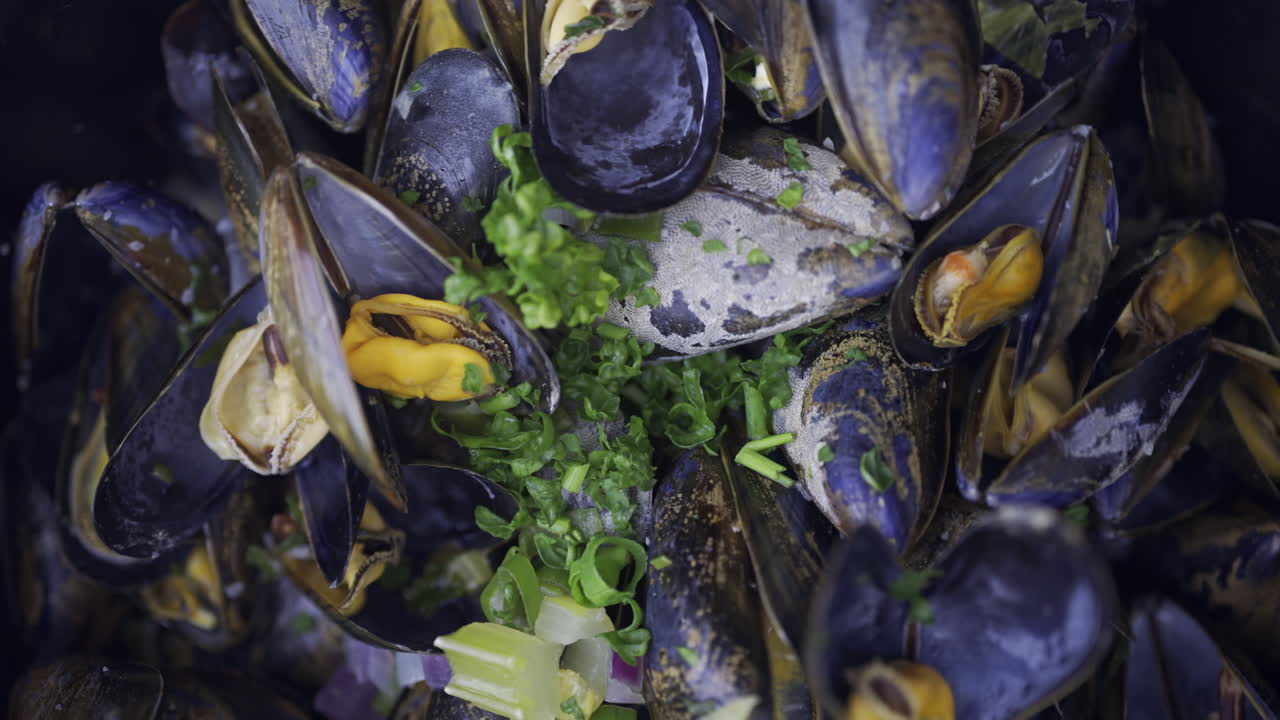 Close up of multiple steamy mussels in a pot with green onions on top