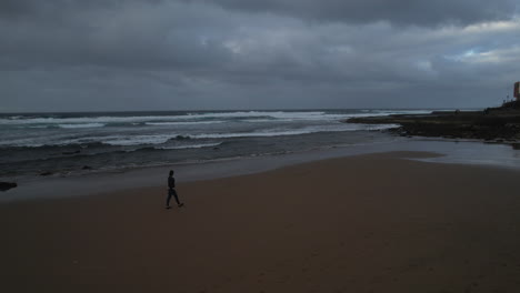 aerial shot of a woman walking along the shore during sunset, on the beach of boca barranco in the city of galdar, on the island of gran canaria