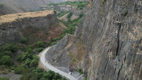 aerial: tourists walk path below garni canyon basalt rock cliff