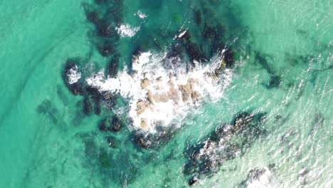 drone aerial top view of waves breaking into some rocks in the middle of the pacific ocean