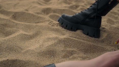 girl legs wearing black boots lying seashore sand close up. woman sitting beach.