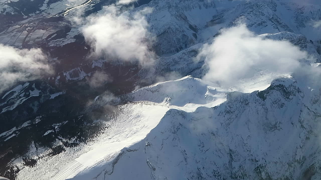Footage looking down through clouds over the snowy alps