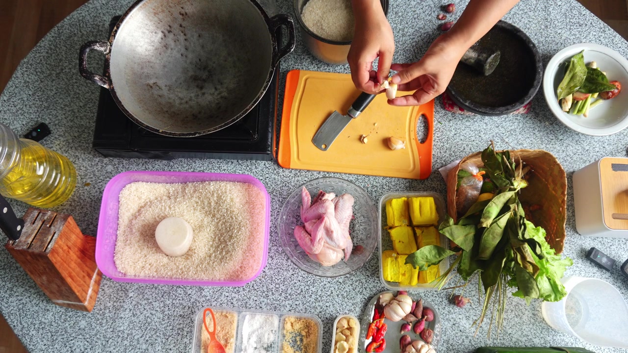 Pemandangan dari atas koki mengupas dan mengiris siung bawang putih di atas talenan oranye selama persiapan dapur