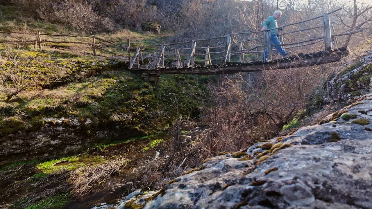 Man walks steadily over a risky decaying river trail wooden footbridge