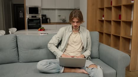 relaxed man sitting on sofa working from home on laptop