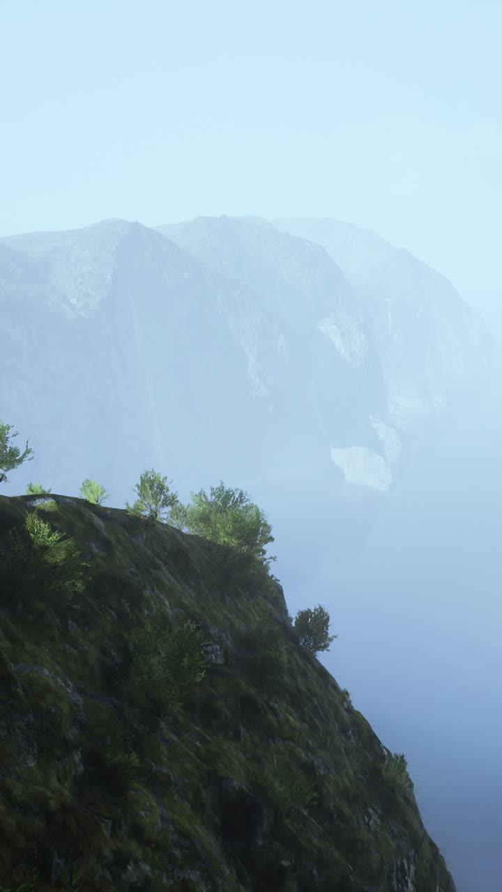 un paisaje montañoso brumoso con árboles altos en un acantilado escarpado