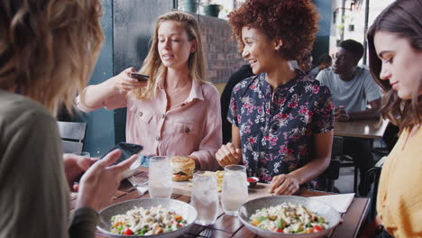 four female friends taking photos of food in restaurant to post on social media