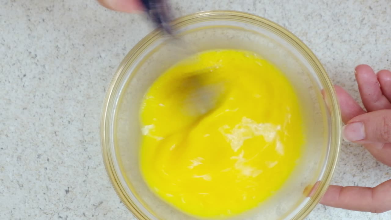 Woman beating eggs with a fork in a glass bowl
