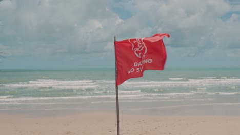 Empty-tropical-sandy-beach-with-Red-flag-waving,-Danger,-No-Swimming-Prohibition,-Cloudy-weather