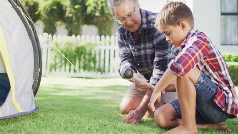 Happy-caucasian-grandfather-and-grandson-pitching-tent-together-in-garden,-slow-motion