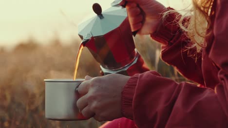 hands woman tourist poured hot coffee from coffee pot into mug of bright warm sunrise in meadow in mountains. tourist makes transition in mountains meets dawn of sun. lens flare. loop. camping, hiking