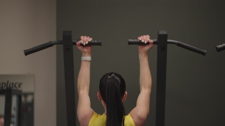 Hispanic Woman Does Pull-Ups On Gravitron For Strengthening The Shoulder Muscles In The Gym. A woman does the exercises correctly pulling up with a straight back. pull-ups on the simulator