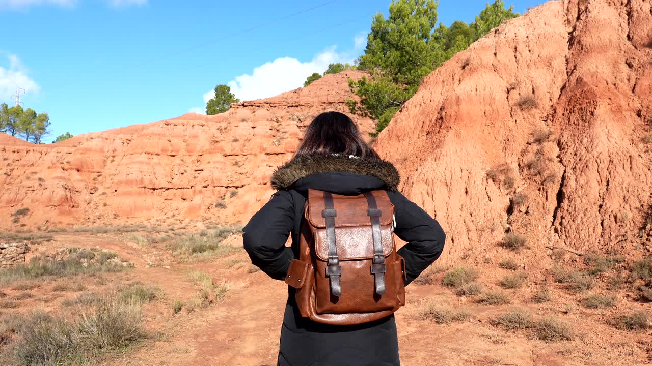 Donna con zaino che cammina attraverso un paesaggio desertico di roccia rossa.