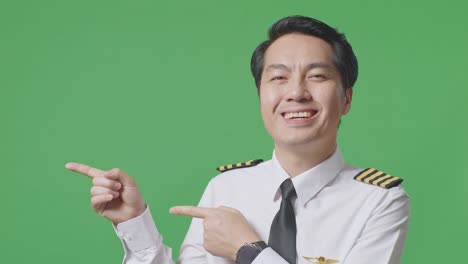 close up of asian man pilot smiling and pointing to side while standing in the green screen background studio