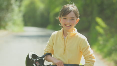 Portrait-Of-Girl-With-Skateboard-Walking-Along-Country-Road