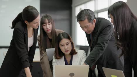 in a meeting room, a group of coworkers are staring at laptops and conversing.