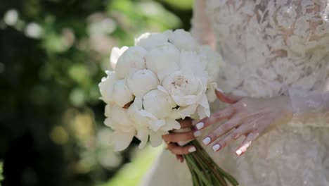 charming bride in a white dress holding a wedding bouquet of white roses or peonies flowers