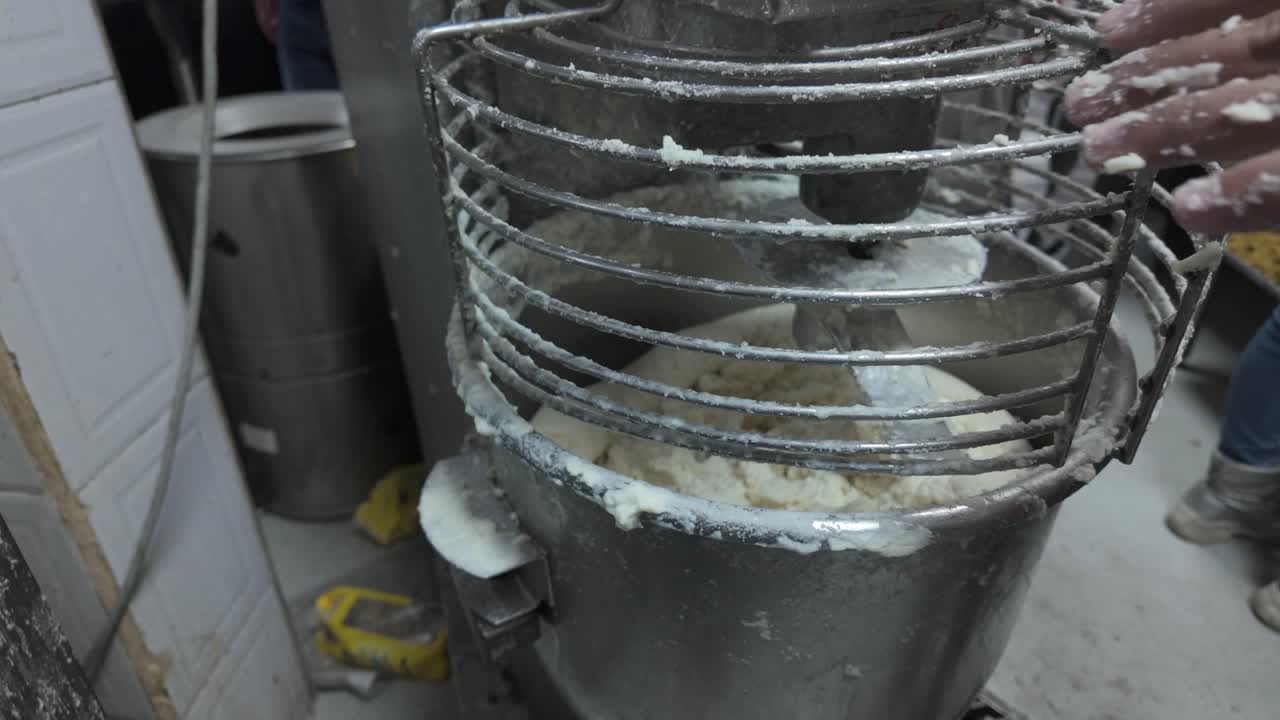 Primer plano que detalla la consistencia espesa y blanca de la masa de maíz para hacer arepas o tamales, que se está mezclando de forma eficiente en una cocina profesional de gran volumen