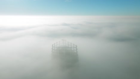 aerial view: drone glides backward, revealing a solitary skyscraper emerging through dense sunrise clouds in the quiet cityscape