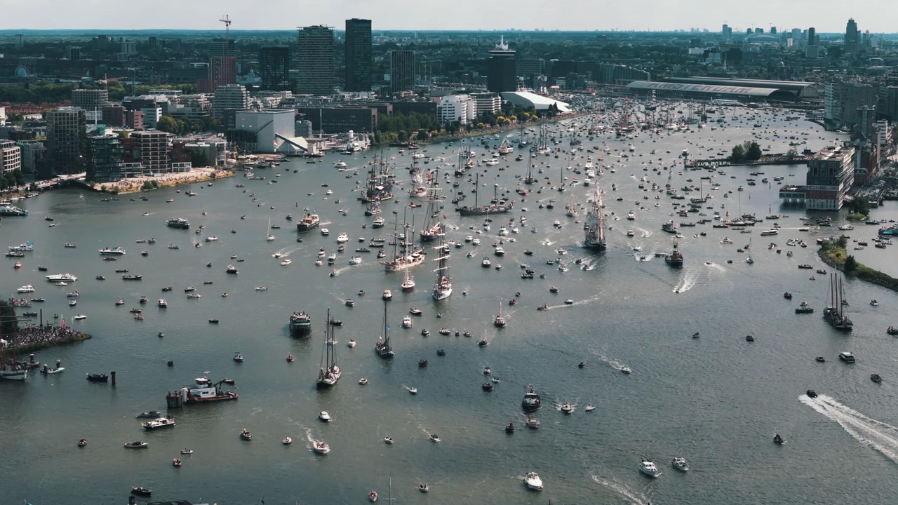 Drone approaches and pans right over sailboats departing Amsterdam