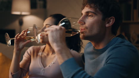 relaxed lovers drinking wine in cozy apartment interior at night close up.