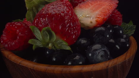 Fresh-rotating-forest-berries-in-a-wooden-bowl,-wet-bright-fruits,-strawberries,-blueberries,-raspberries,-4K-macro-shot