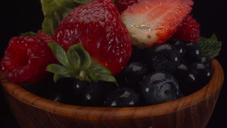 bayas de bosque rotativas frescas en un cuenco de madera, frutas brillantes húmedas, fresas, arándanos, frambuesas, tiro macro de 4k