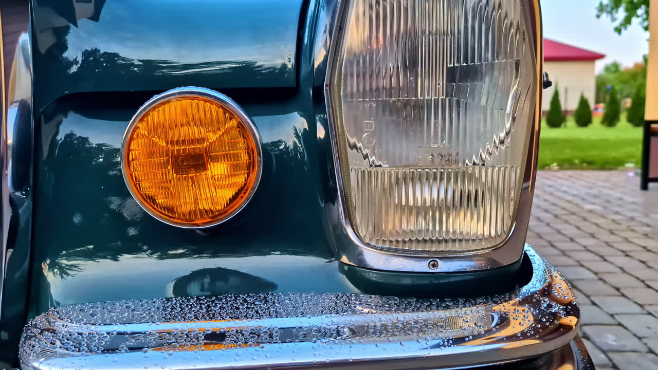 A Vintage Car’s Front Headlight and Amber Signal Light With Raindrops on the Bumper - Zoom In Shot