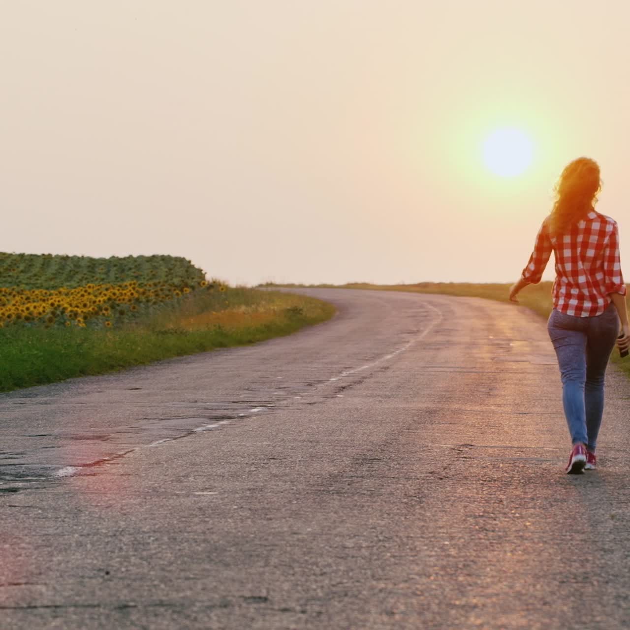 一位女士在日落时沿着乡村路向前走