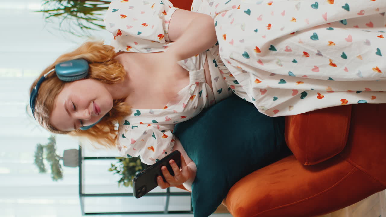 Giovane donna felice con le cuffie wireless che si rilassa sdraiata sul divano a casa ascoltando la sua musica preferita