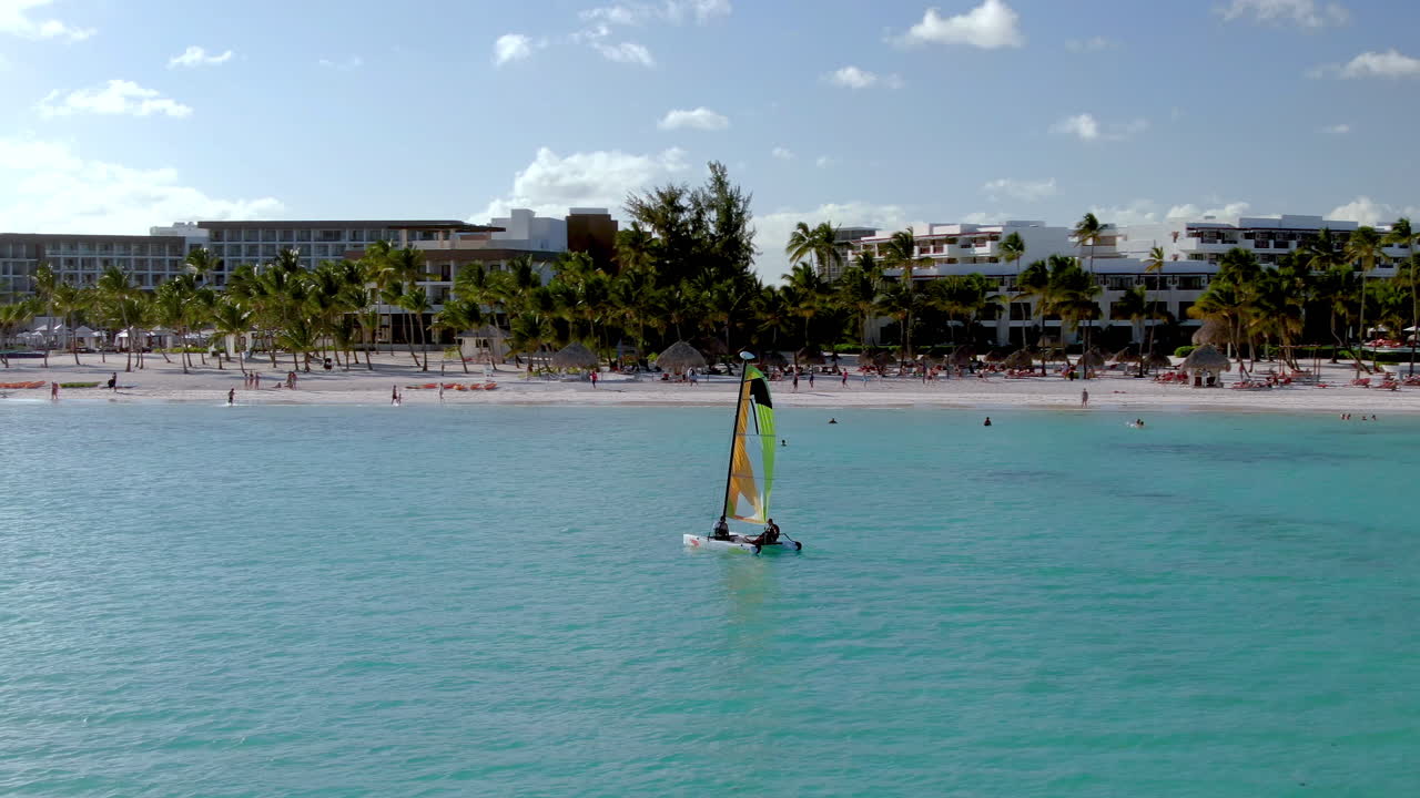 Segeln in der Karibik vor der Küste von Punta Cana, Dominikanische Republik, mit luxuriösem Urlaubs- und Ferienresort im Hintergrund, weißem Sandstrand und Palmen