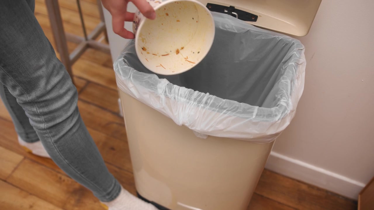 Woman open rubbish bin with her leg and throws plastic container, slow motion