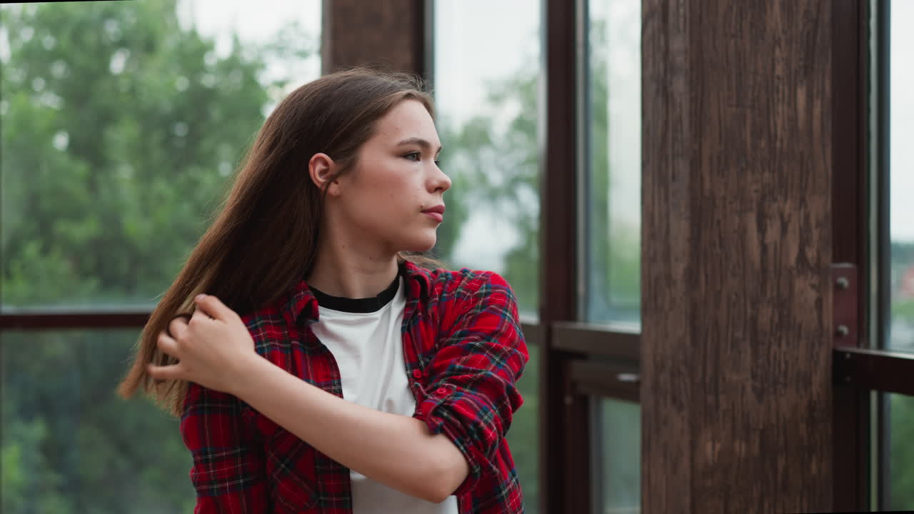 여자의 손가락은 귀 뒤에 느슨한 머리카락을 고, 여성의 섬세한 몸짓은 파노라마 창문 근처에서 내성적 감각과 조용한 성찰의 감각을 전달합니다.