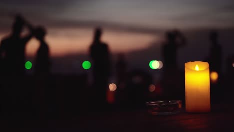 yellow candle on the table with blurred people walking on the beach during sunset on background