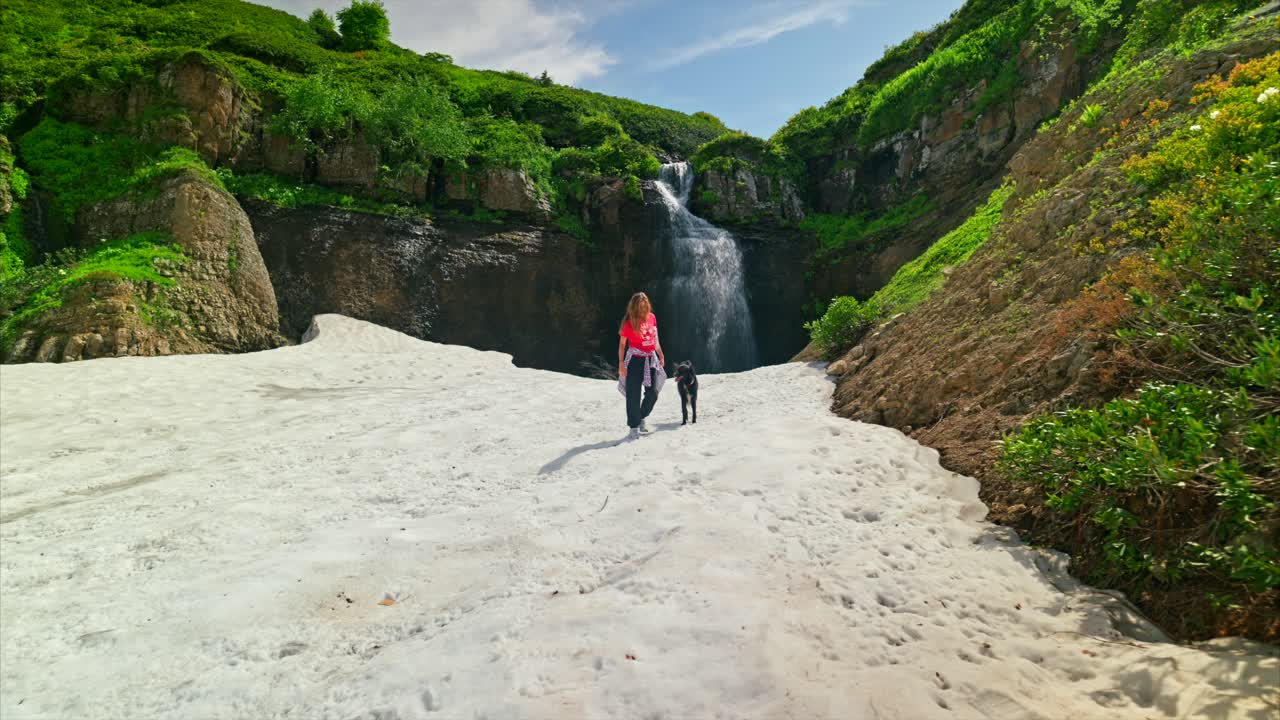 una mujer y su perro disfrutando de un paisaje nevado con una hermosa cascada en el fondo