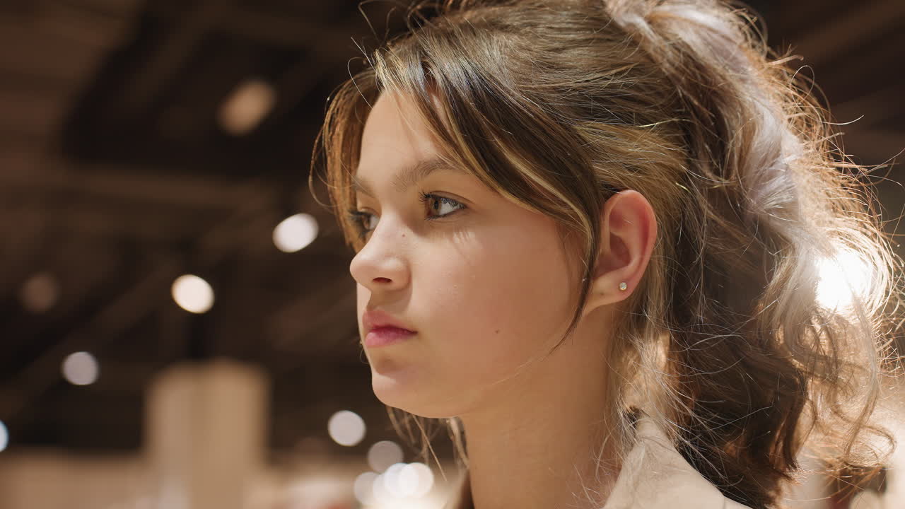 부드러운 쇼핑몰 조명 아래 청초한 인물 사진, 쇼핑몰 조명 아래 후광 머리를 가진 십 대 소녀, 어둑한 보케 조명 아래 사려 깊은 표정을 짓고 있는 어린 소녀