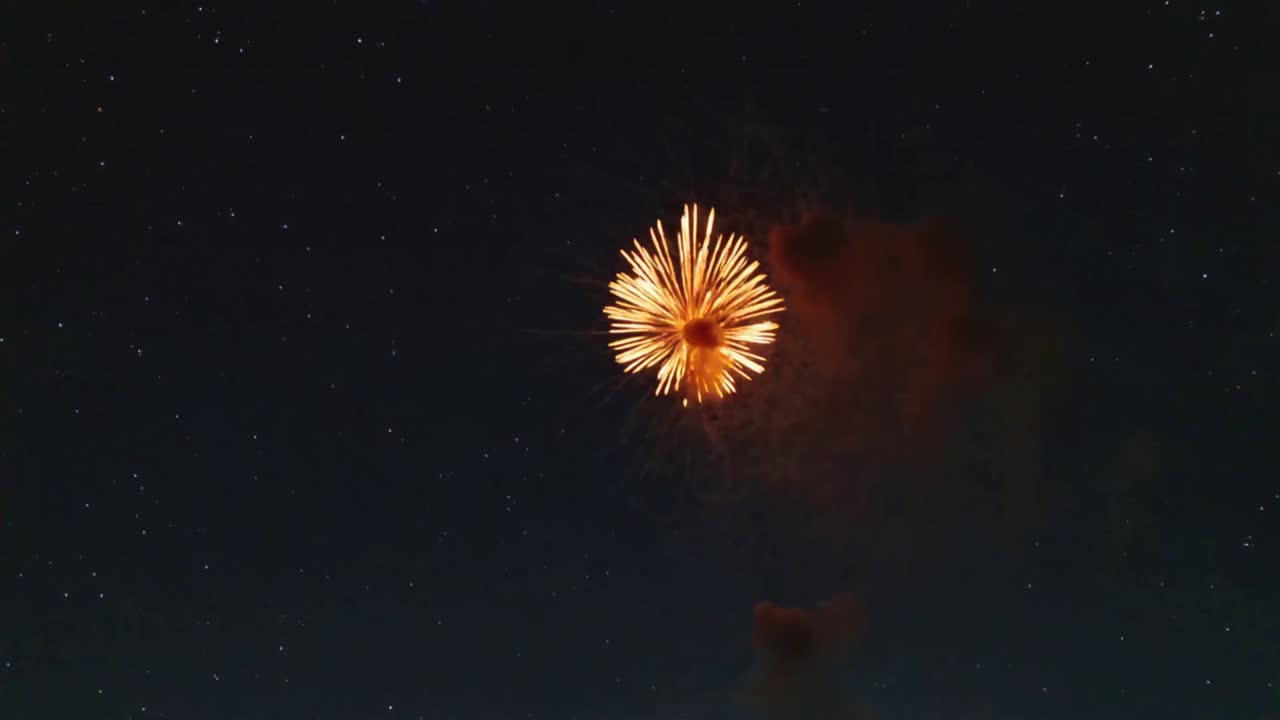 Esplosione di una shell pirotecnica che crea un anello di scintille a forma di cuore dorato sopra un campo, con l'obiettivo di formare un cuore con il fumo